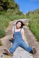 A woman in overalls sitting on the side of a road.