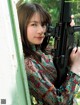 A woman holding a rifle leaning against a wall.