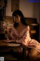 A woman in a pink kimono sitting at a table with a glass of water.